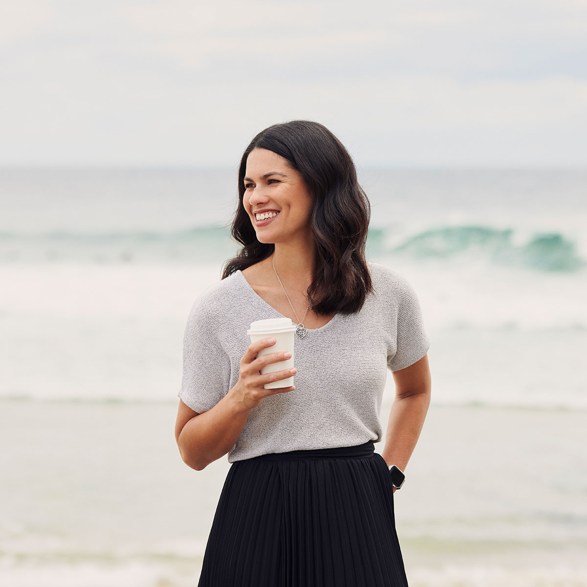 Lisa smiling on beach with coffee in hand