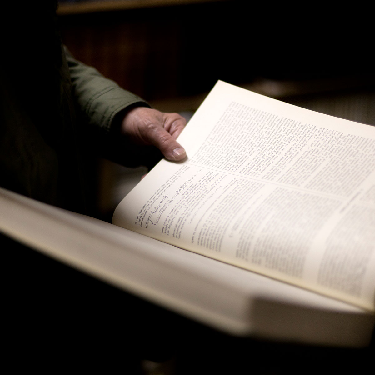A person holds a large textbook in one hand in a dimly lit room.