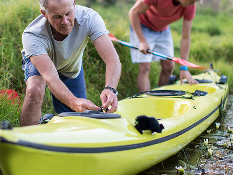 Elderly man rigging up a kayak with a friend