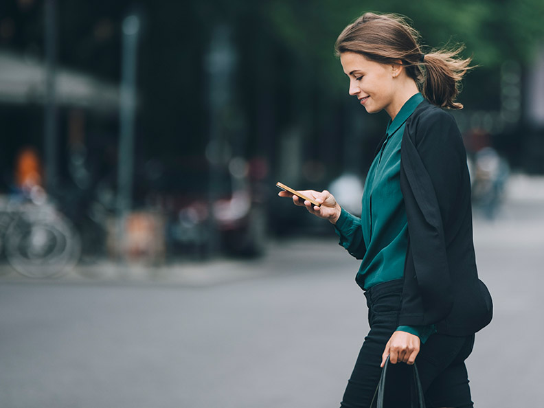 Confident businesswomen using smart phone while crossing street in city