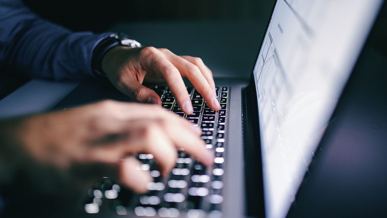 Close up of hands typing on laptop with a bright screen light