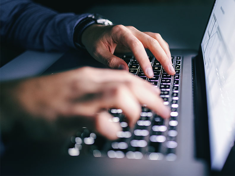 Close up of hands typing on laptop with a bright screen light