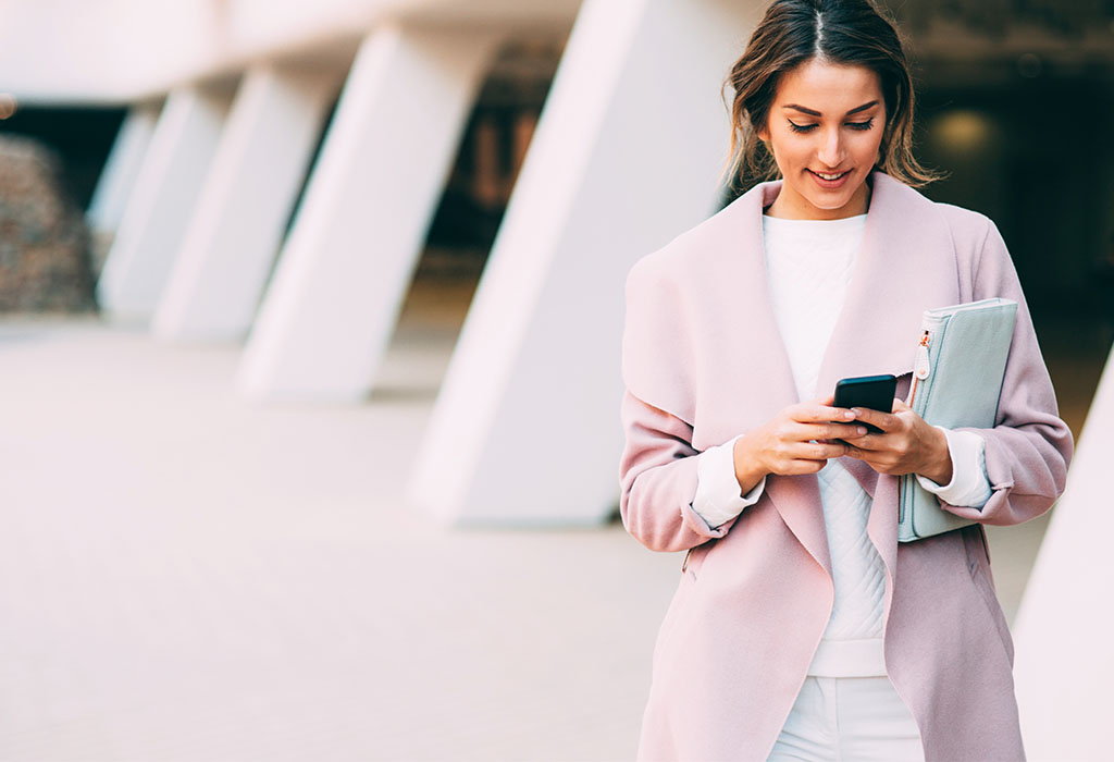 A well dressed young woman texting on the phone on her way to the train station.