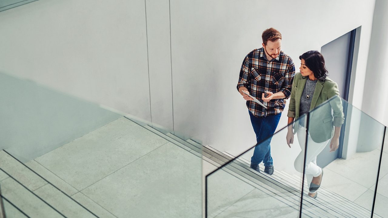 Two young coworkers using tablet walking up stairs