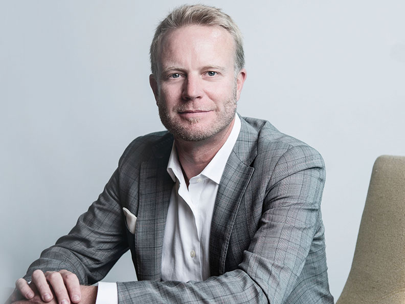 A business man in a suit in a grey meeting room. Macquarie - Cameron Garrett