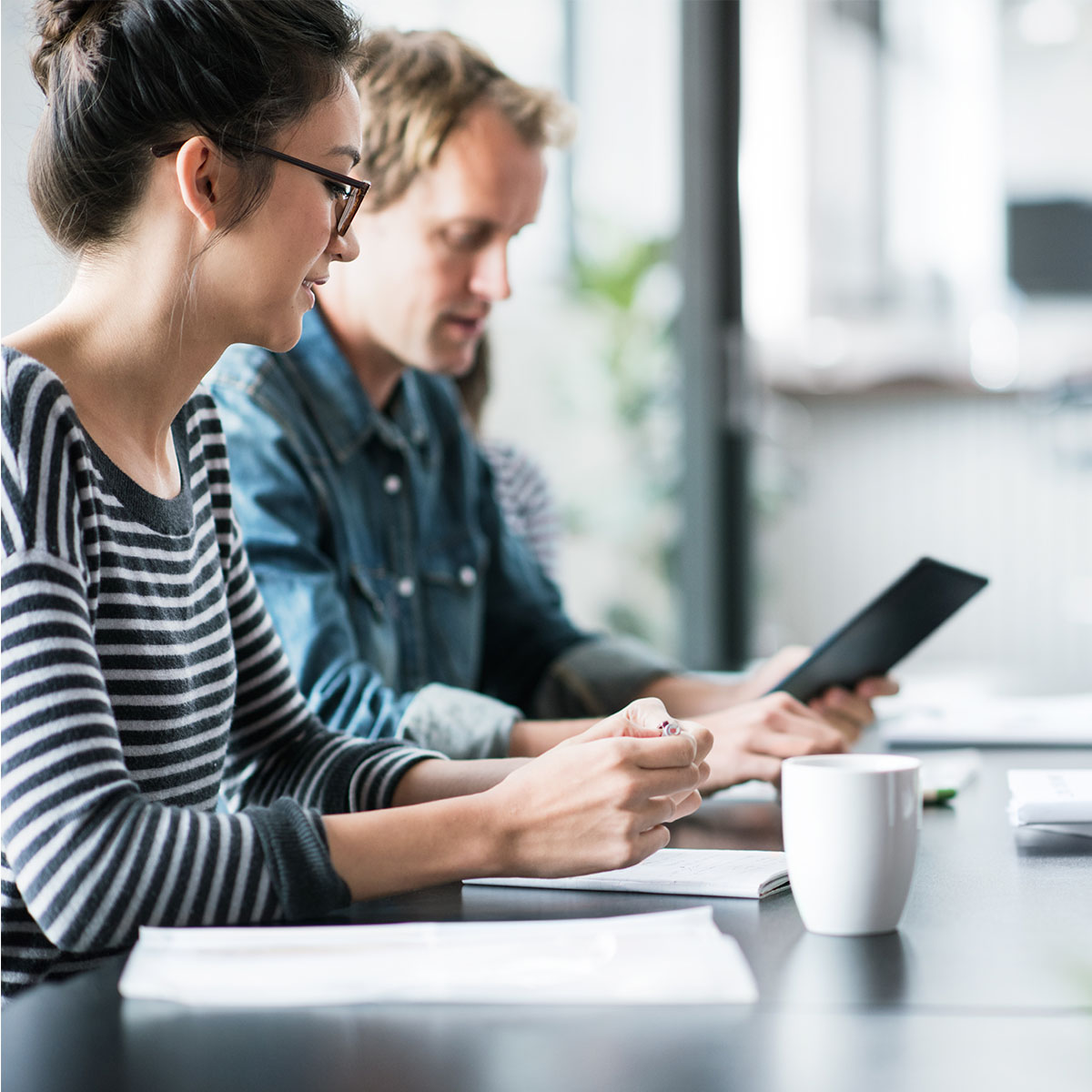 Two people looking over documents on a tablet with a coffee in an office meeting room.
