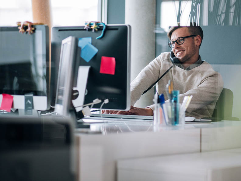 Business professional typing notes with keyboard on computer while talking and smiling on the phone to client.