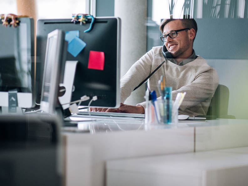 Business professional typing notes with keyboard on computer while talking and smiling on the phone to client.