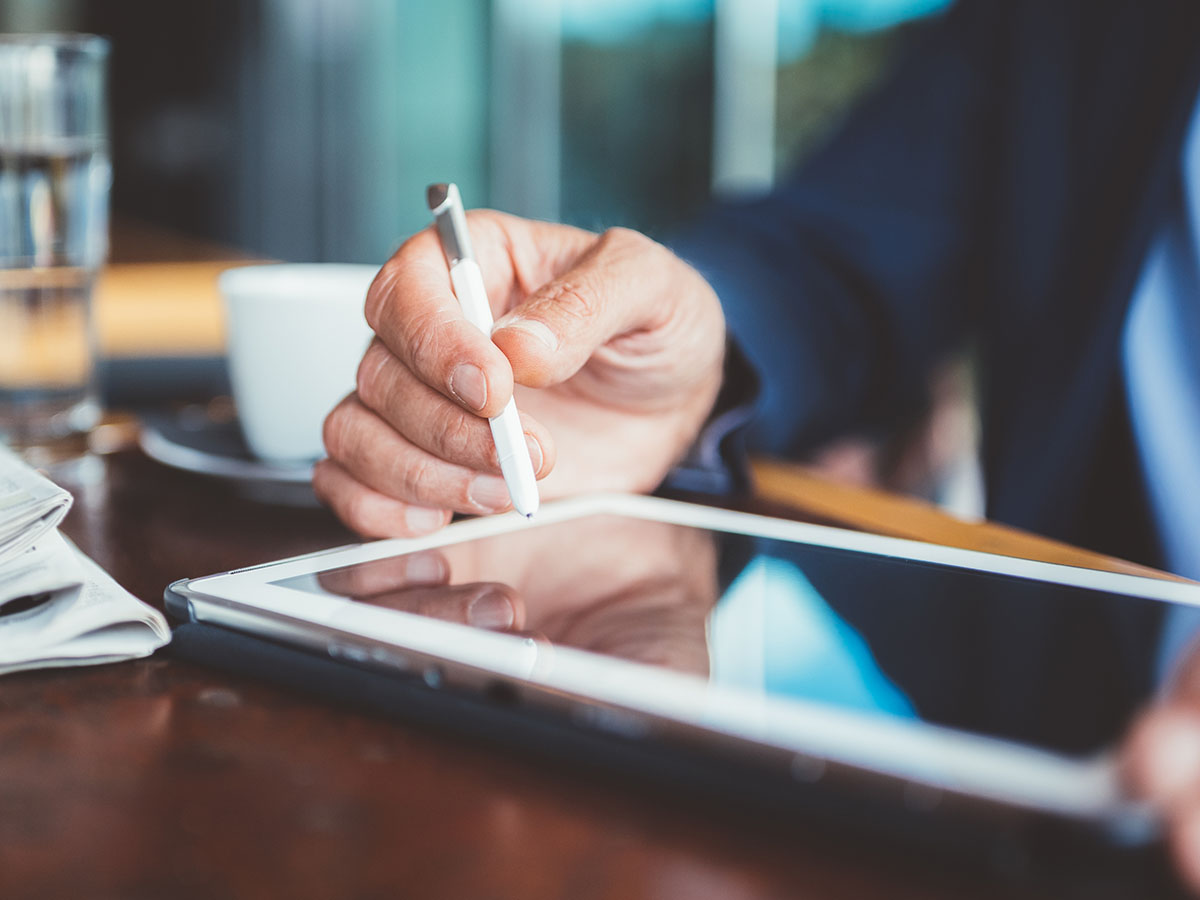 Hand holding a tablet writing on a tablet outside at a cafe