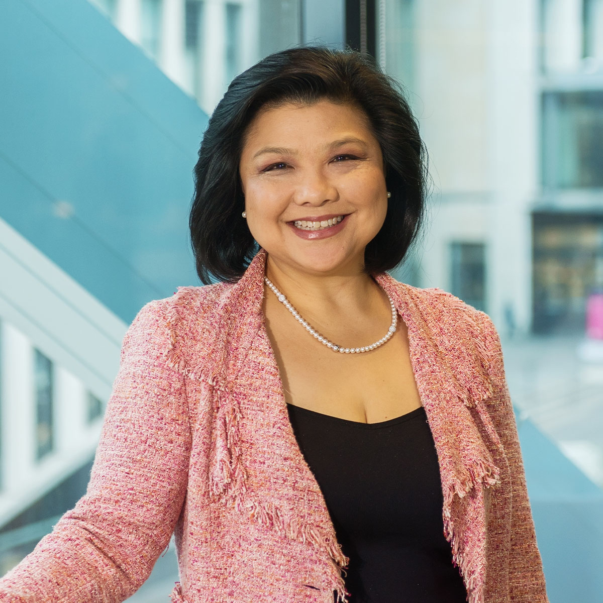 A business woman in a pink blazer standing in front of a large window in a modern office. Macquarie - Margaret
