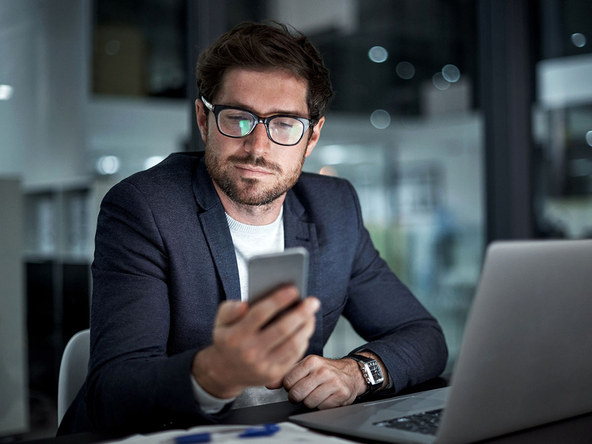 Young businessman using his laptop and phone at work in a dark office