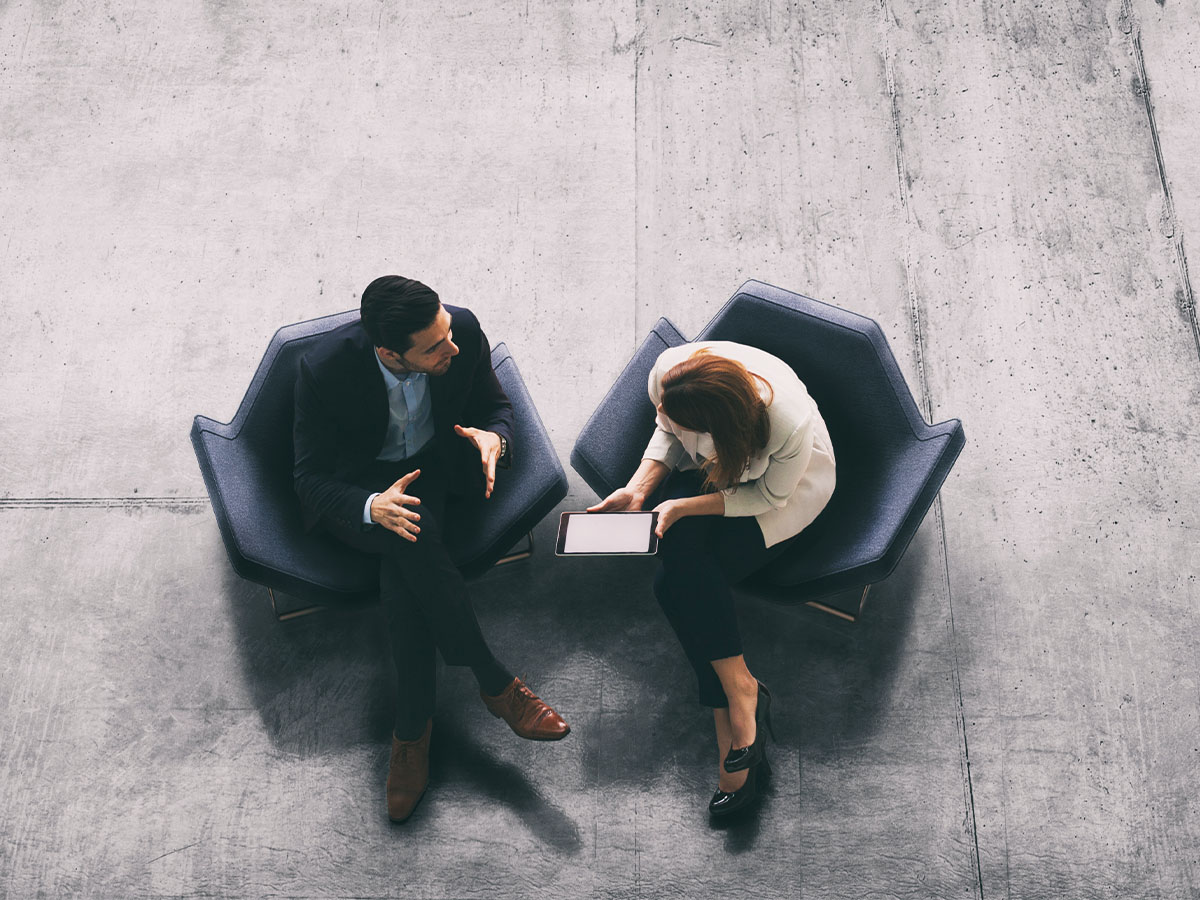 A high-angle view of a businessman and a businesswoman sitting in the office building lobby and using a digital tablet