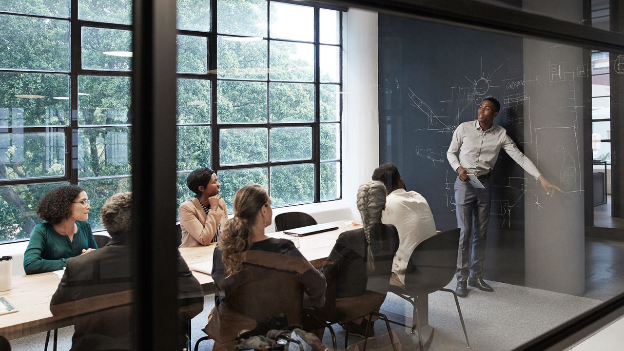 Businessman explaining while male and female colleagues sitting in conference room seen through glass wall at workplace