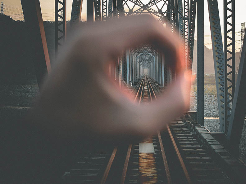 Cropped Hand Forming Circle In Front Of Railway Bridge