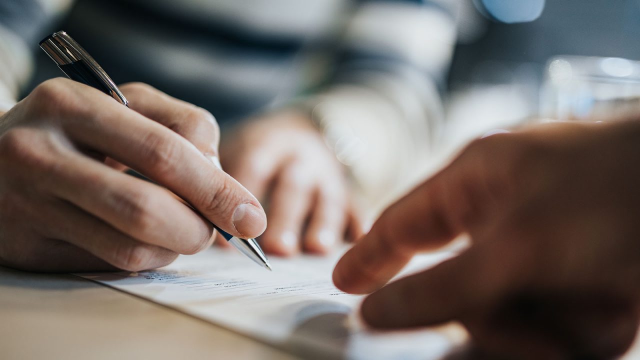 Close-up of businesswoman's hand holding a pencil pointing at a brochure with a businessman in meeting.