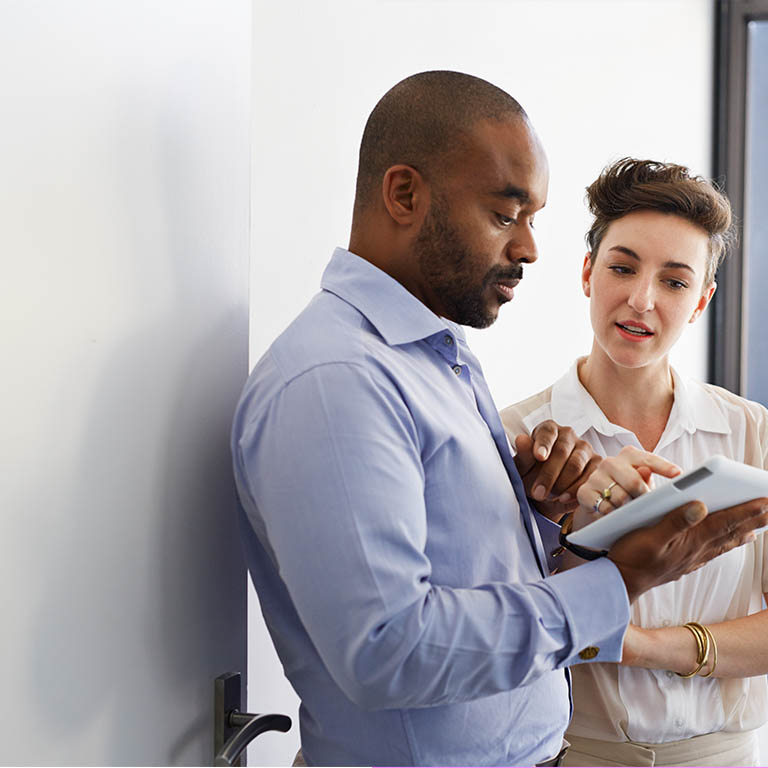 Business man and woman discussing over a digital tablet at work in a bright white room.