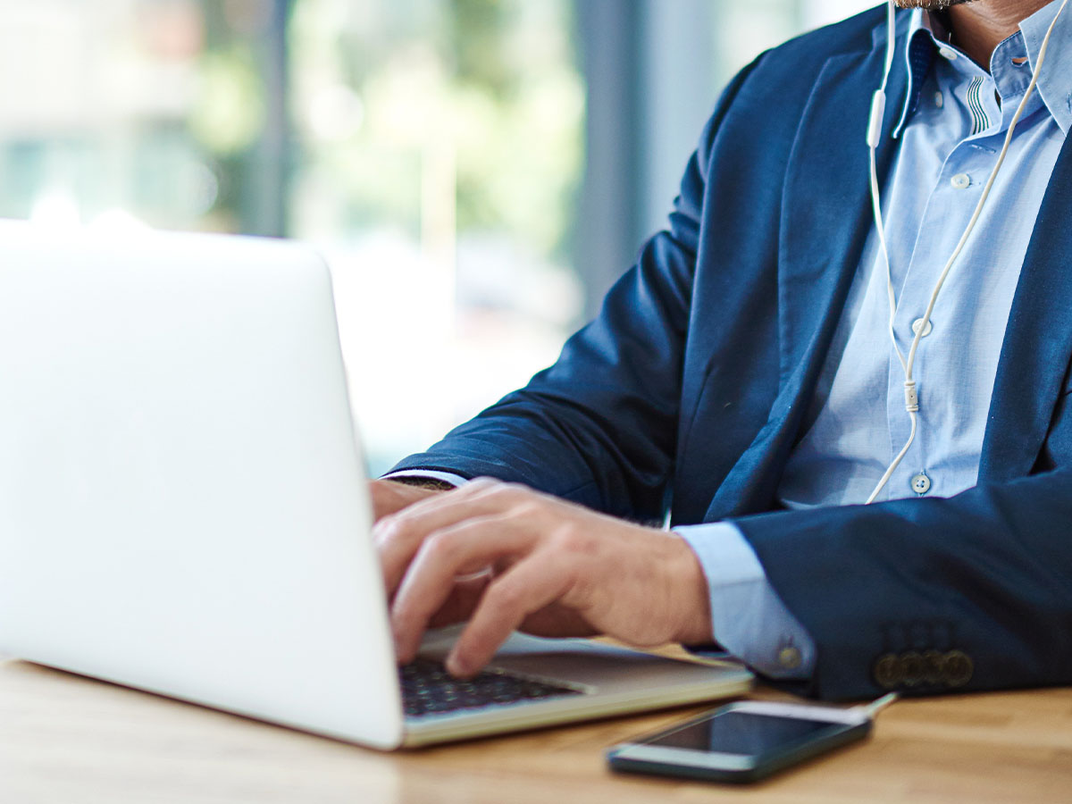 Medium shot of a mature businessman wearing earphones while using his laptop at work