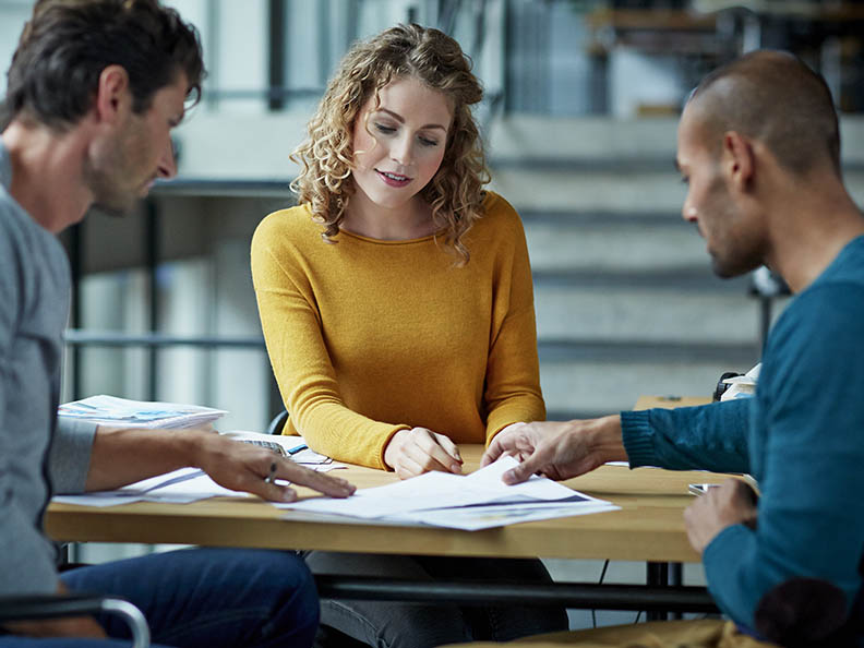 Three people casually discussing over paperwork in office enviornment