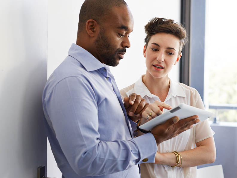 Business man and woman discussing over a digital tablet at work in a bright white room.