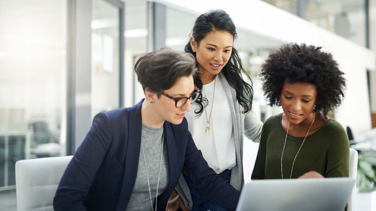 3 multi-ethnic business women meetng around a laptop in an office.