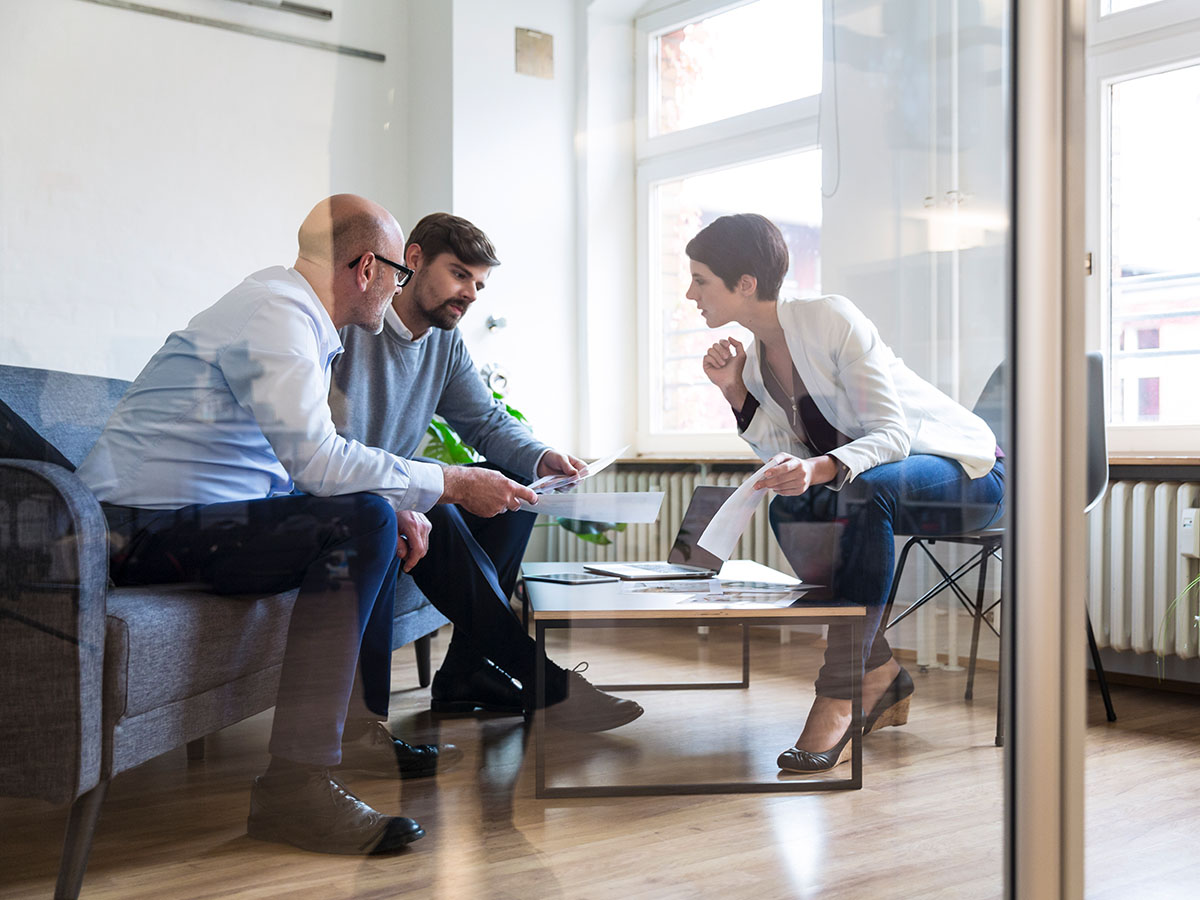 Three colleagues, two male and one female sitting in a casual boardroom having a meeting during the day.