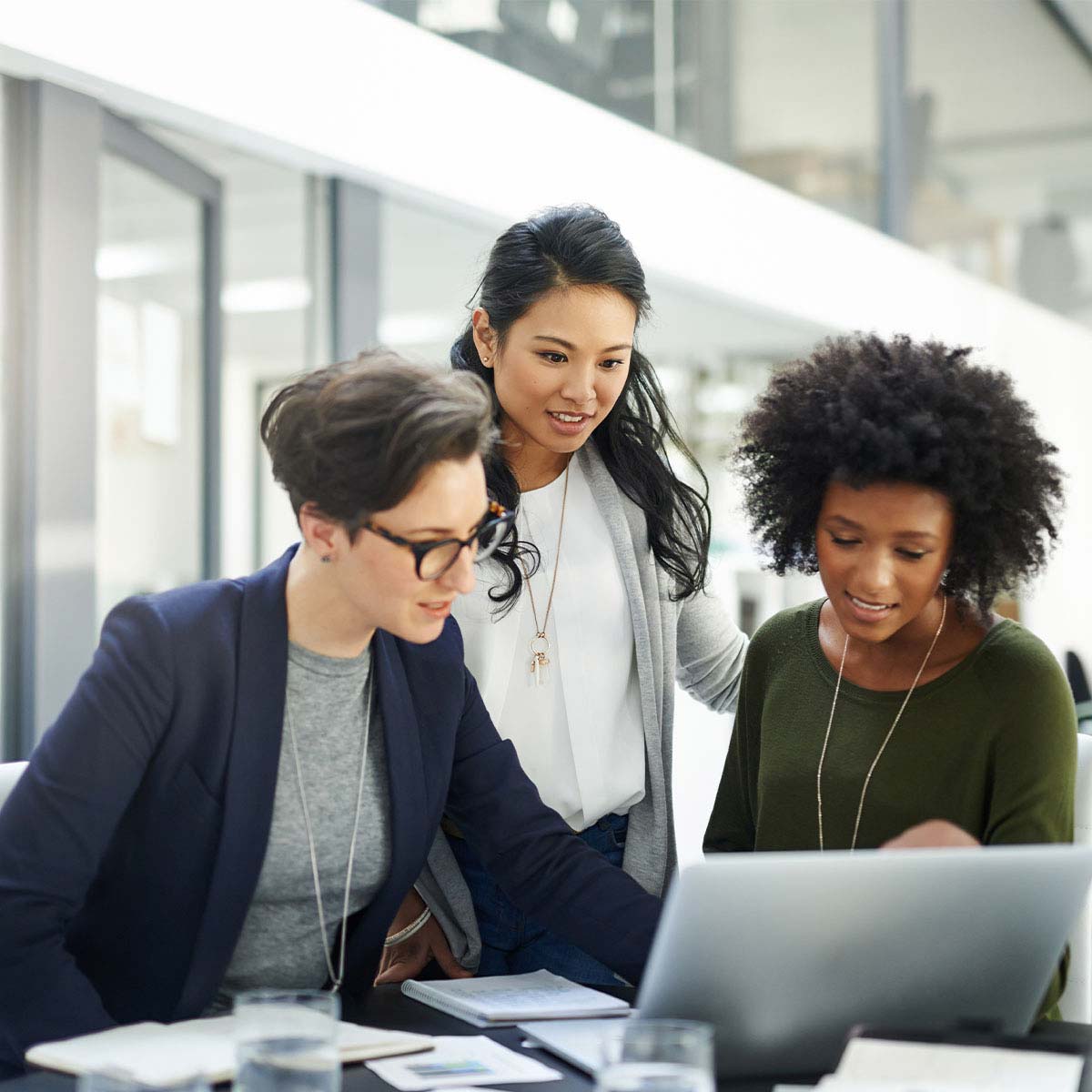 3 multi-ethnic business women meetng around a laptop in an office.