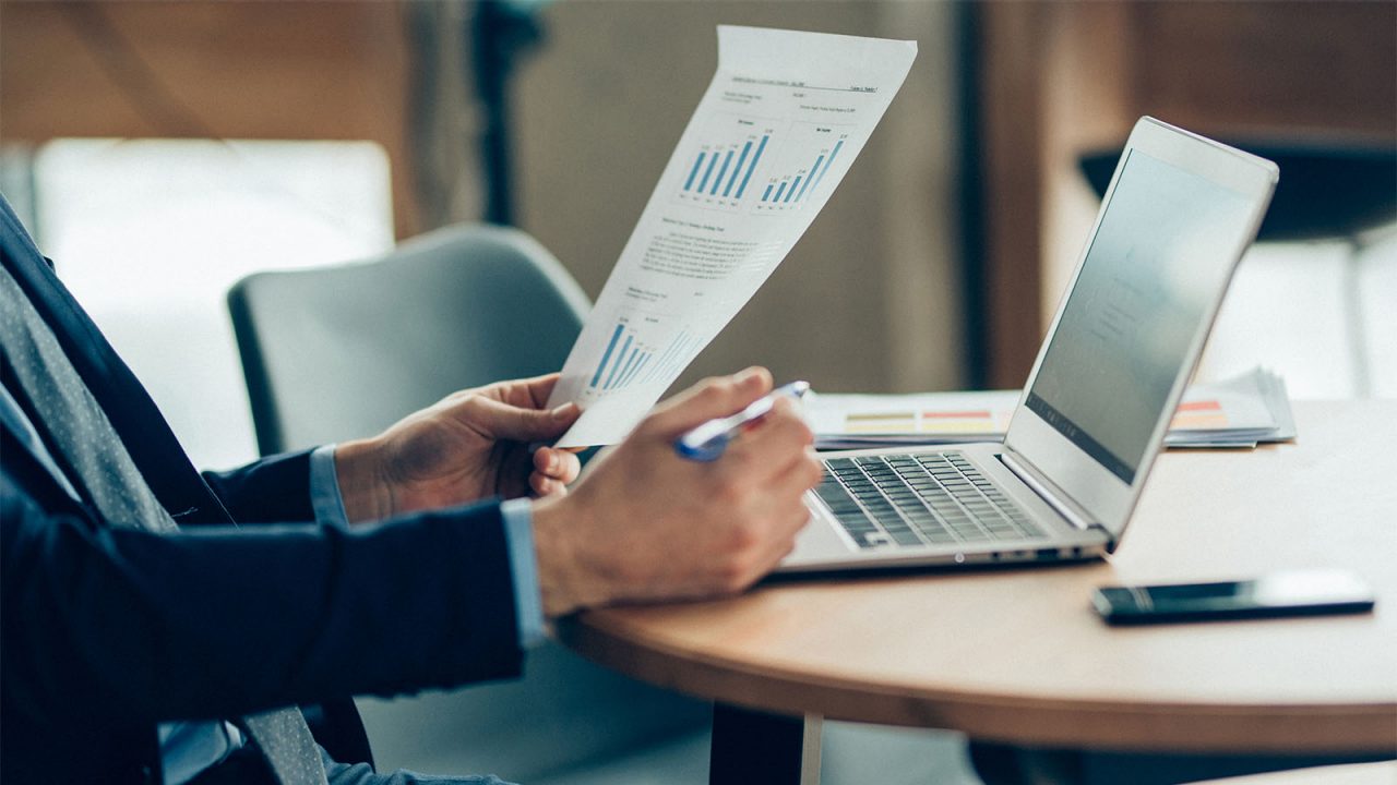 Close shot of hands of businessman with a laptop and documents workin at a round table.