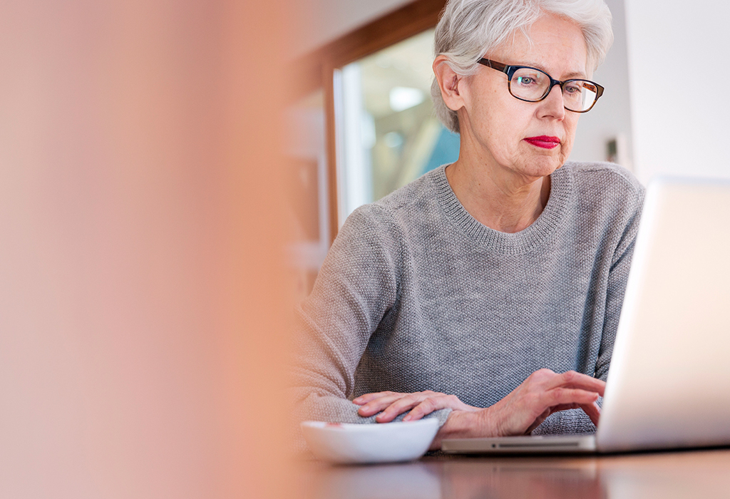 Mature woman with glasses on laptop in casual setting.