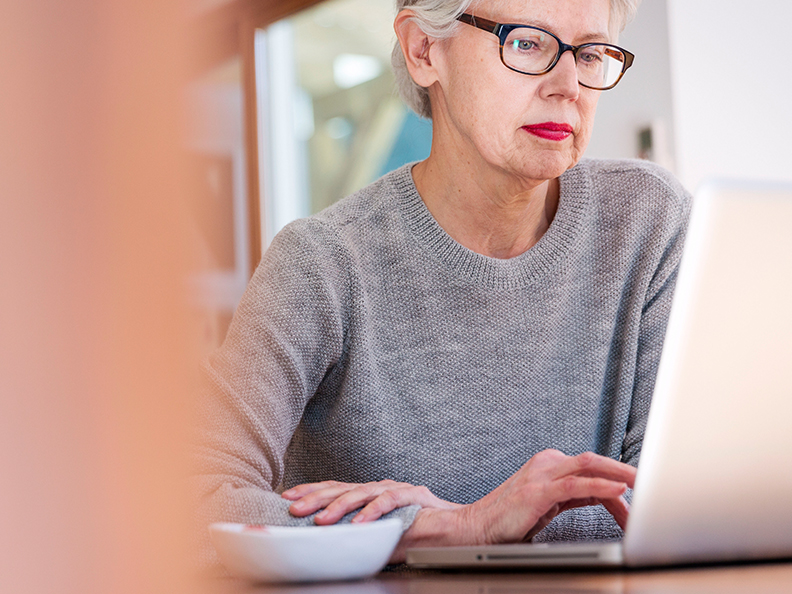 Mature woman with glasses on laptop in casual setting.