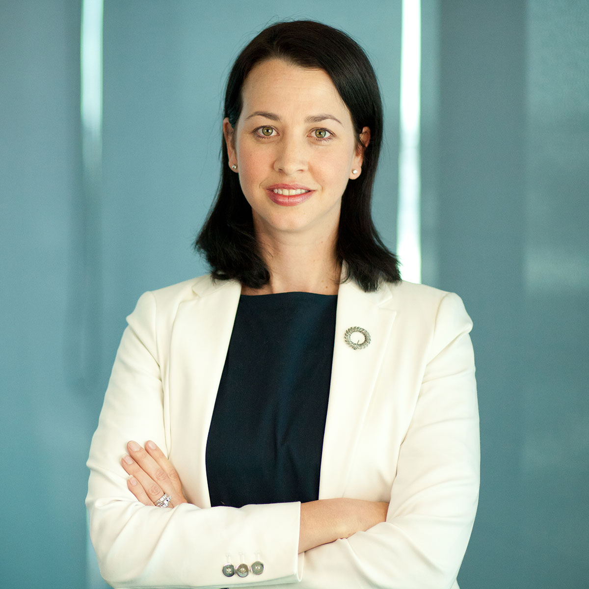 A business woman dressed professionally in a white blazer standing with her arms crossed, looking at the camera.
