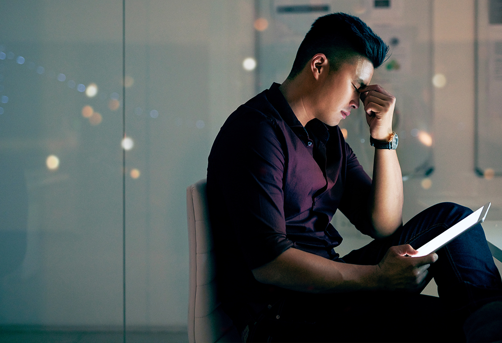 Shot of a young asian man looking stressed while using a digital tablet at night in a modern office