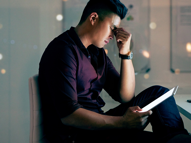 Shot of a young asian man looking stressed while using a digital tablet at night in a modern office