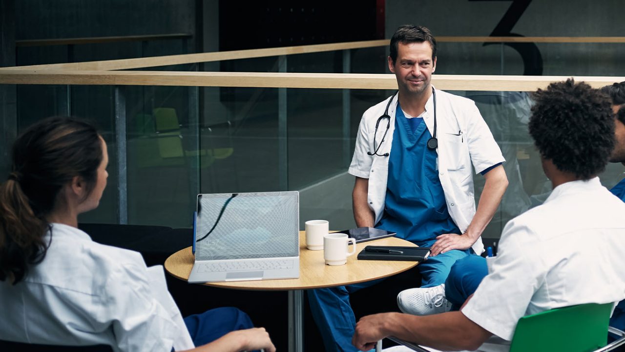 Shot of a group of medical staff seated around a table drinking coffee and having a discussion inside a hospital