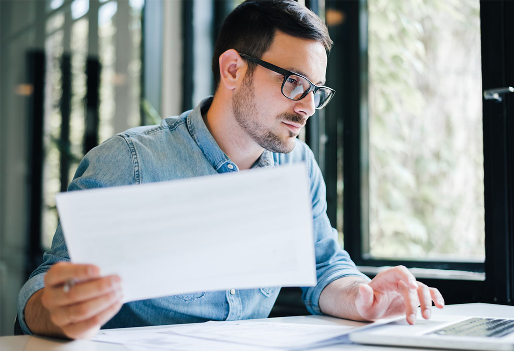 Focused young casual business man in office looking at documents and working with laptop