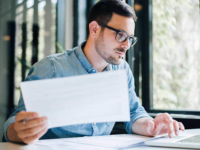 Focused young casual business man in office looking at documents and working with laptop