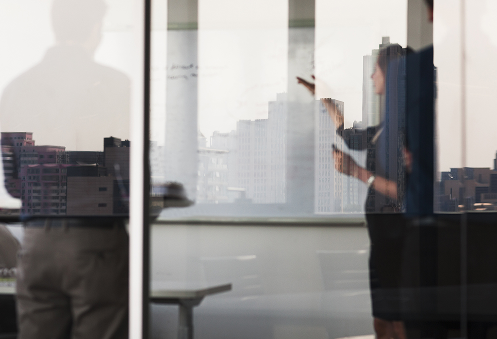 Reflection into meeting room with business woman presenting to white board.