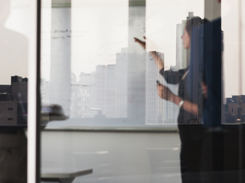 Reflection into meeting room with business woman presenting to white board.