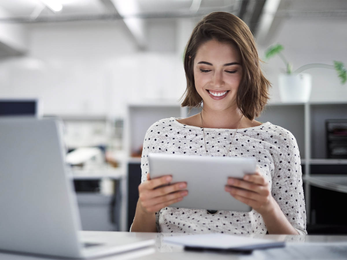 A young woman holding and looking at a tablet in a modern office
