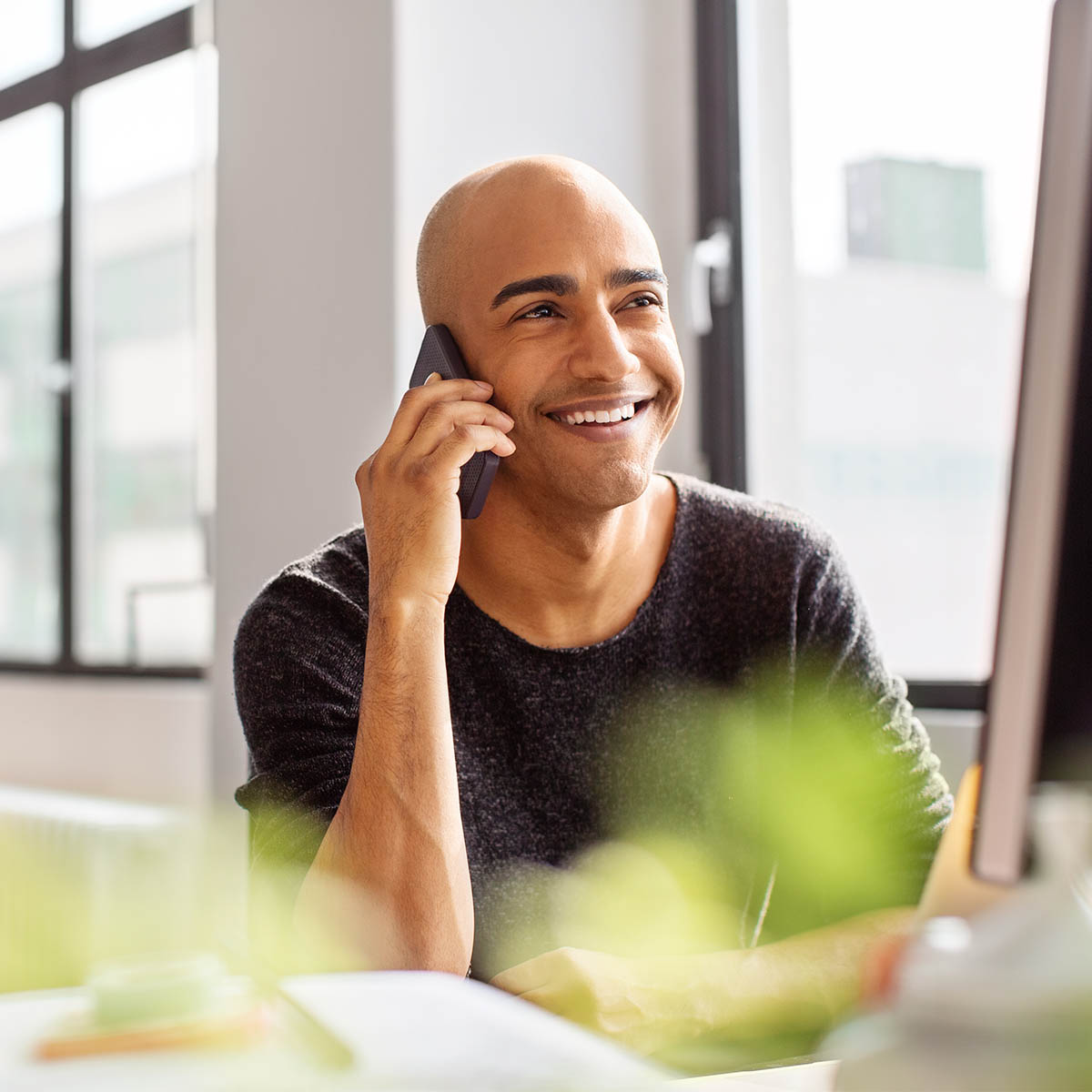 A man sitting at a desk smiles as he takes a phone call on his mobile.