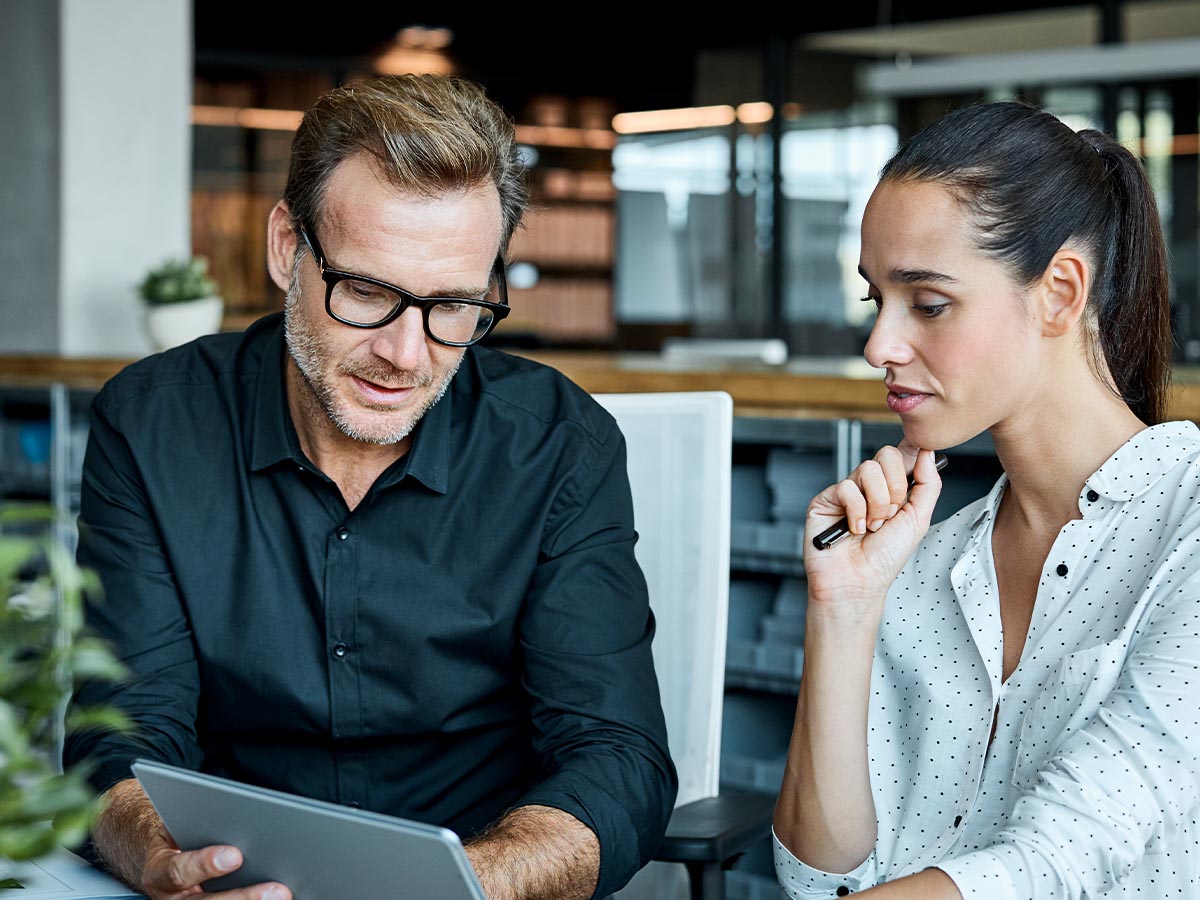 A male and female colleague looking at a tablet in a well lit office.