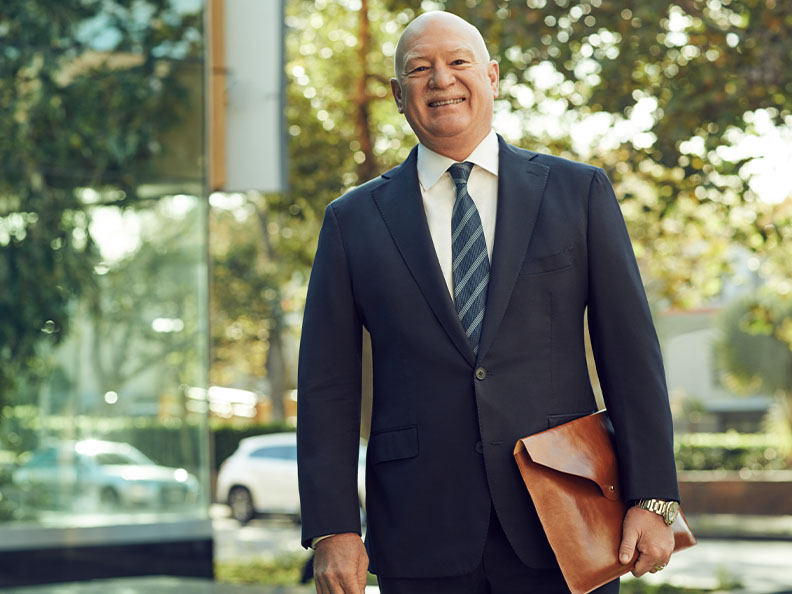 A businessman in a suit standing outside smiling as he holds some documents in his hand on a sunny day. Macquarie - Craig