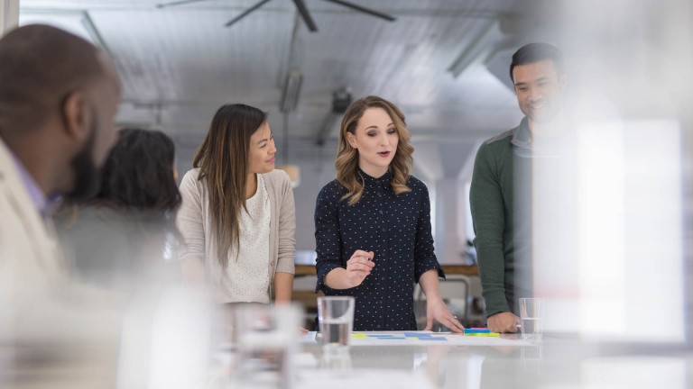 People in a team standing around a desk and collaborating in office