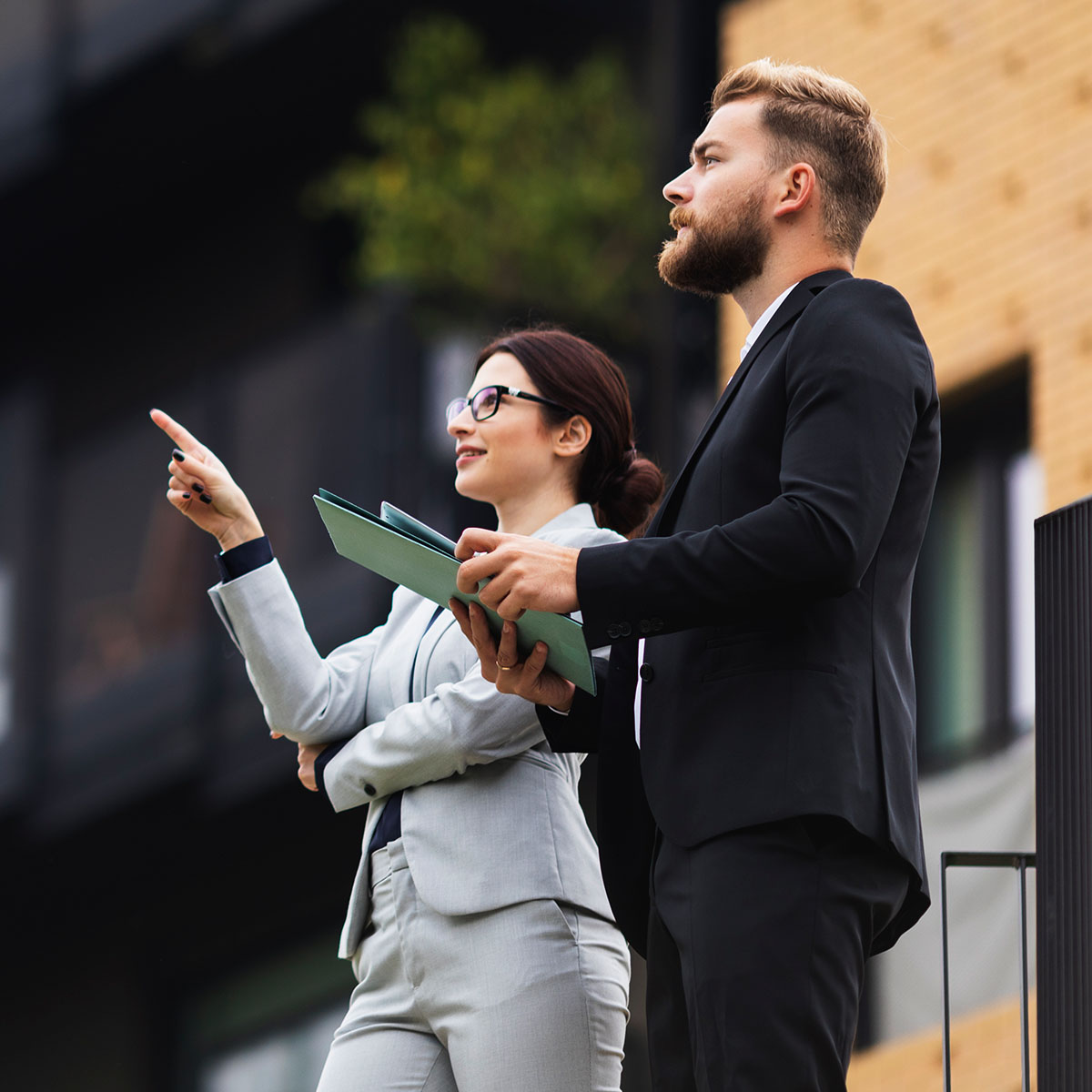 A business woman points something out to her colleague outside. Her colleague is holding some documents.