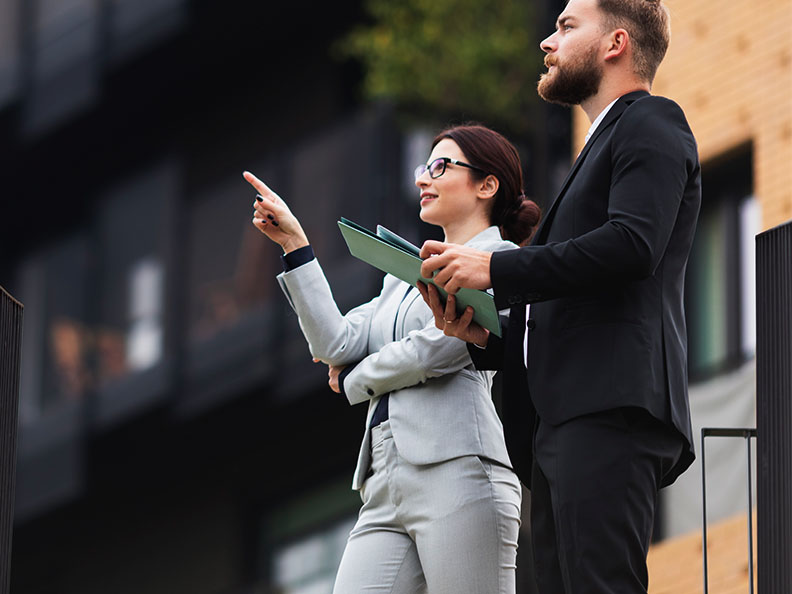 A business woman points something out to her colleague outside. Her colleague is holding some documents.