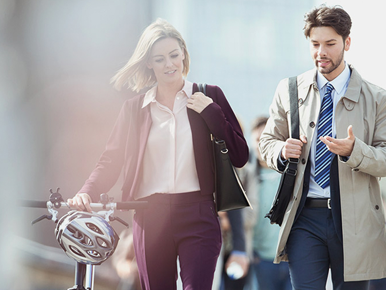 Two people walking to work while talking and holding bike