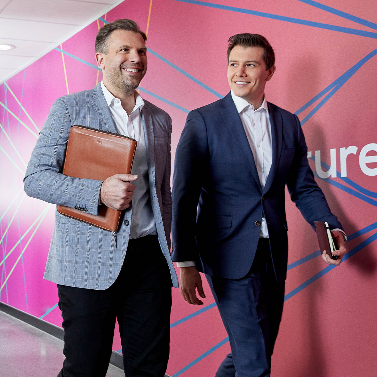 Two men in suits walking down a corridor with a colourful wall behind them. Macquarie customer - ReadyTech