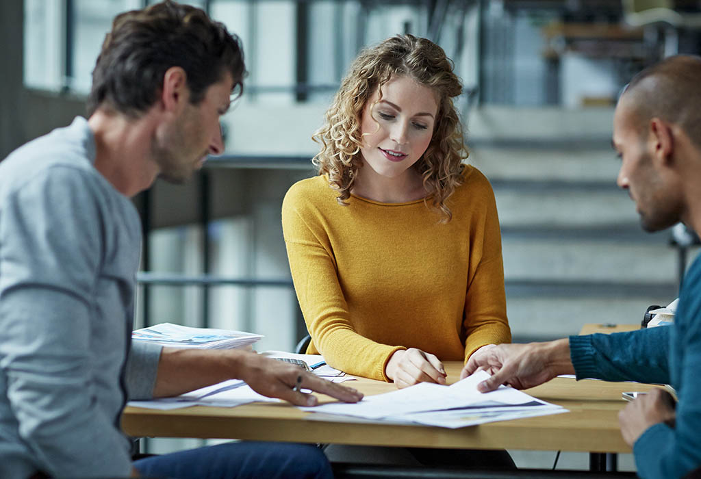 Three people casually discussing over paperwork in office enviornment