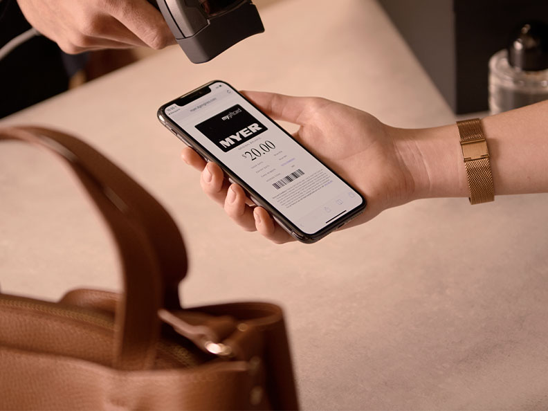 In a retail store a person uses a scanner on a phone showing a Myer card via the Macquarie moble app