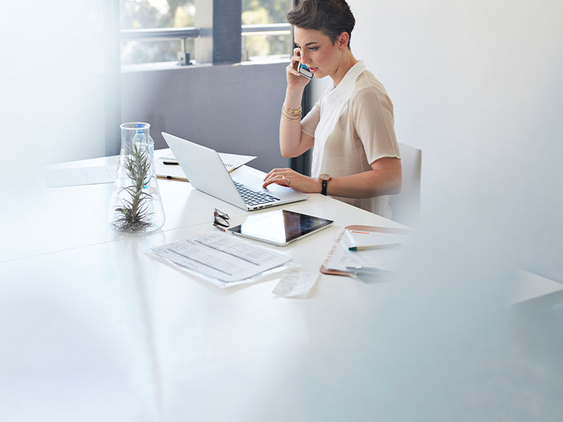 Businesswoman on the phone & in front of laptop, shot through glass