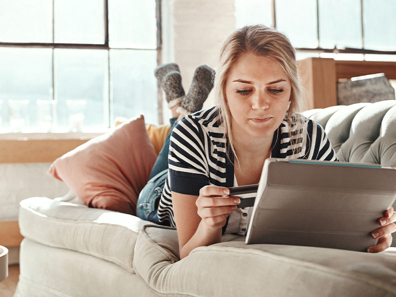Shot of a young woman relaxing on the sofa and using a credit card with a digital tablet